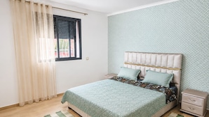 A bedroom with a bed, a nightstand, a window with curtains, and patterned wallpaper. - Family Comfort House 77 (Témara)