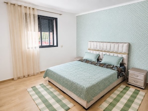 Een slaapkamer met een bed, een nachtkastje, een raam met gordijnen en behang met een patroon.
