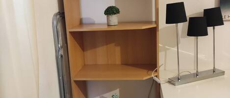 A corner of a room with a wooden shelving unit, a small potted plant, and a white desk with three black lamps.