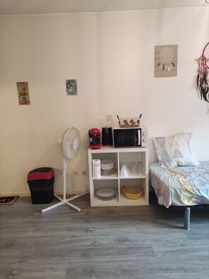 A bedroom with a bed, a white dresser, a microwave, a fan, and a trash bin. - LE 63 at Les Arènes (Nîmes)