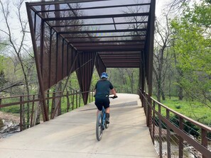 Eine Person fährt auf einem Fahrrad über eine überdachte Brücke mit Metallstreben und einem Betonweg.