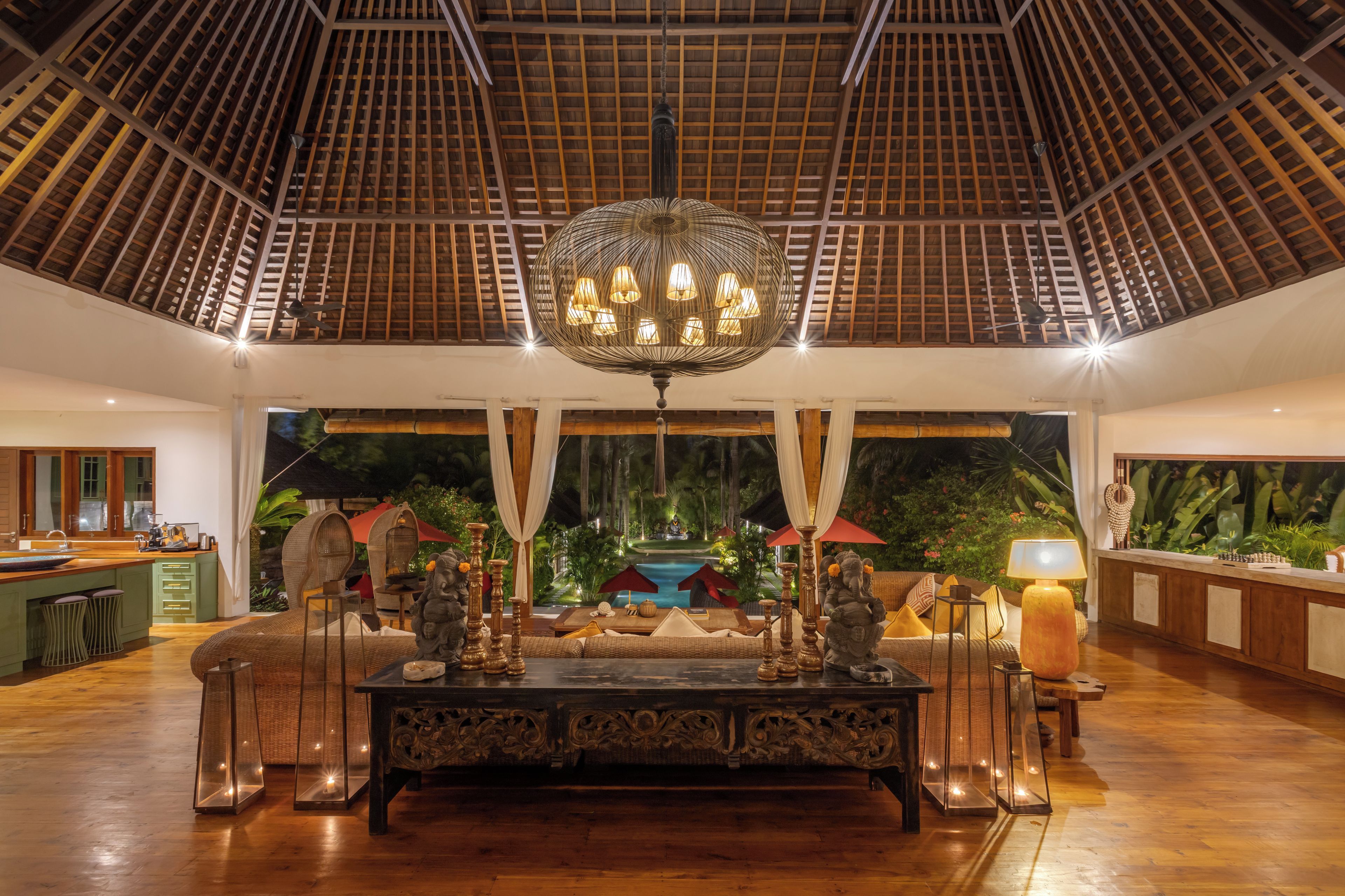 A spacious lobby with a high ceiling, a central ornate table, and a view of a pool and greenery.