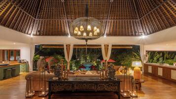 A spacious lobby with a high ceiling, a central ornate table, and a view of a pool and greenery.