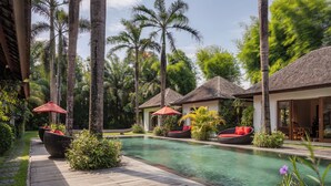 Un área de piscina con sillones de descanso y sombrillas, rodeada de palmeras y una terraza de madera.