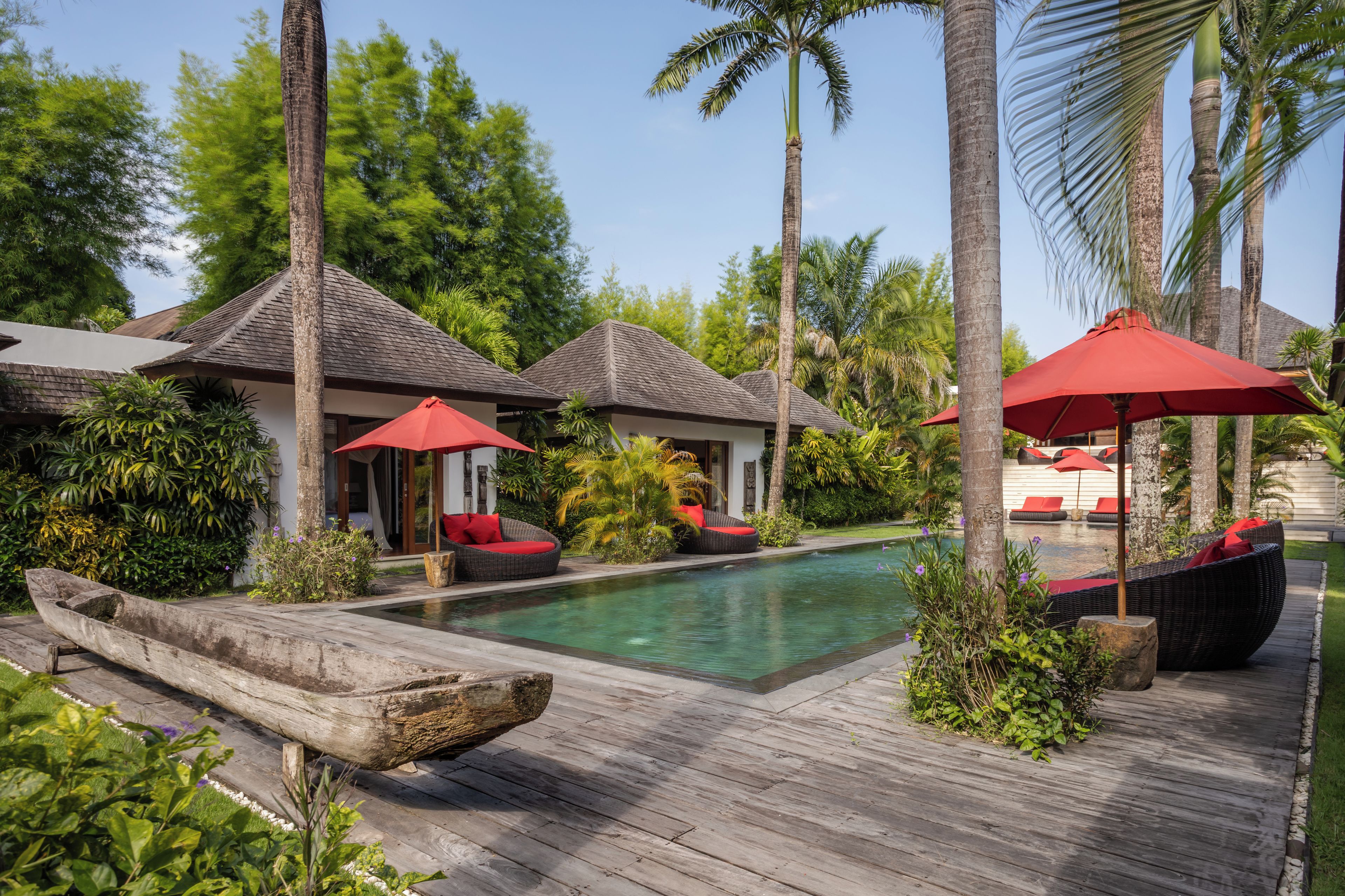 A poolside area with wooden decking, lounge chairs, and umbrellas.