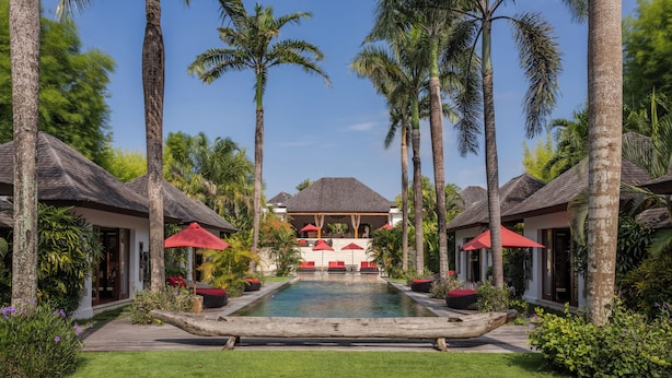 Un resort con piscina central, sillas de descanso y palmeras.