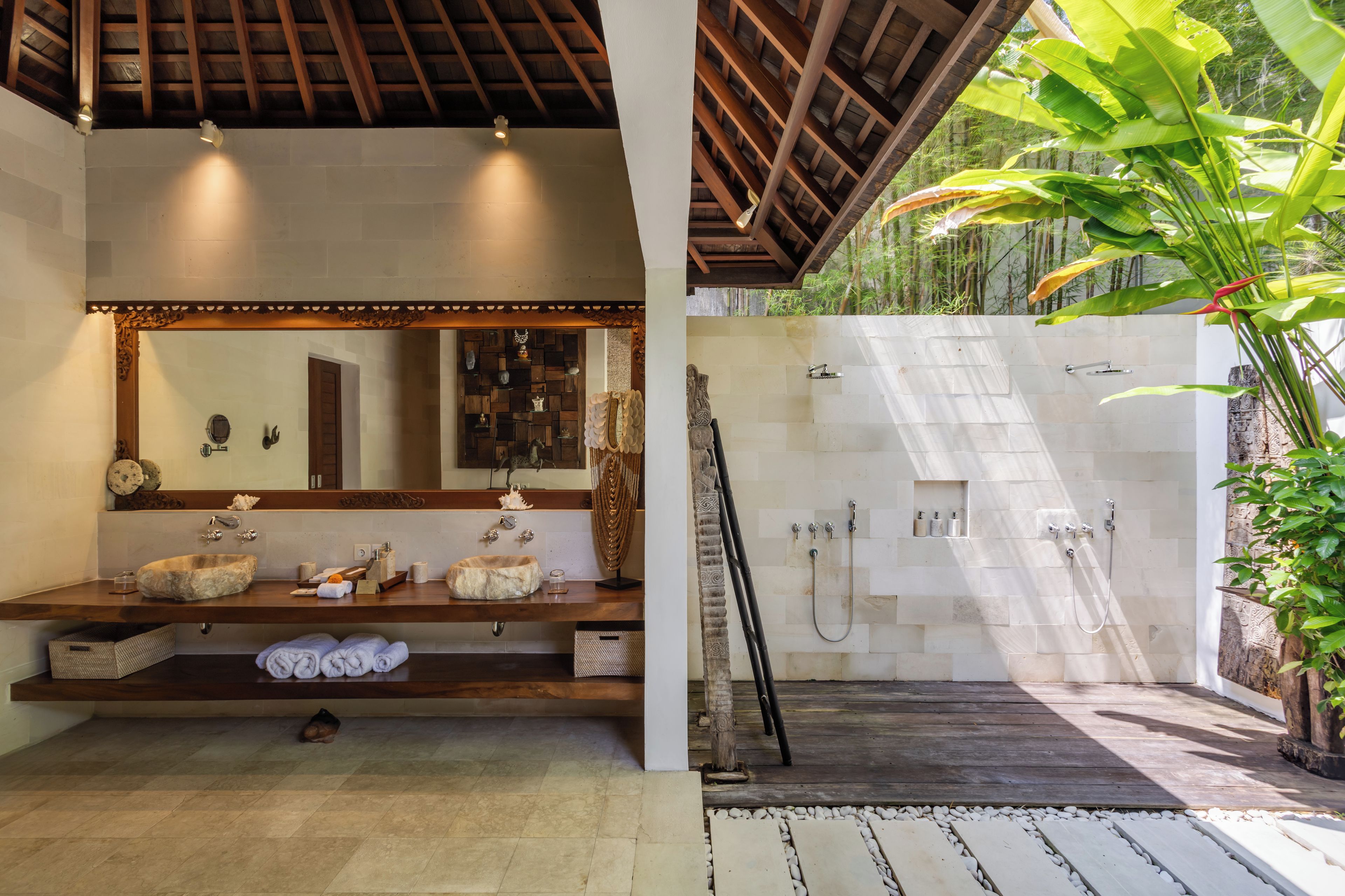 Un baño con tocador de madera, un espejo grande y zona de ducha con pared de azulejos.
