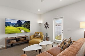 Ein Wohnzimmer mit Flachbildfernseher, einer Couch, einem Couchtisch und einer Lampe.