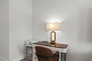 Ein Schreibtisch im Eck mit Lampe, Drucker und Stuhl in einem Zimmer mit weißen Wänden.