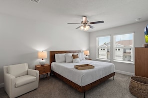 A bedroom with a bed, nightstands, a chair, a ceiling fan, and windows with blinds. - New 2023 Gulf Breeze townhome sleeping 4 across 3 bedrooms, 2.5 baths. King bed, full bunk room, full kitchen, in-unit laundry, dual workspaces & Sonos sound. Minutes to Pensacola Beach, the zoo & Navy bases. Ideal for families or TDY stays. (Gulf Breeze)