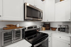 A modern kitchen with stainless steel appliances, including a microwave, oven, and toaster. - New 2023 Gulf Breeze townhome sleeping 4 across 3 bedrooms, 2.5 baths. King bed, full bunk room, full kitchen, in-unit laundry, dual workspaces & Sonos sound. Minutes to Pensacola Beach, the zoo & Navy bases. Ideal for families or TDY stays. (Gulf Breeze)