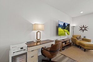 A modern living room with a flat-screen TV, a desk with a printer, a lamp, a chair, and a sofa. - New 2023 Gulf Breeze townhome sleeping 4 across 3 bedrooms, 2.5 baths. King bed, full bunk room, full kitchen, in-unit laundry, dual workspaces & Sonos sound. Minutes to Pensacola Beach, the zoo & Navy bases. Ideal for families or TDY stays. (Gulf Breeze)
