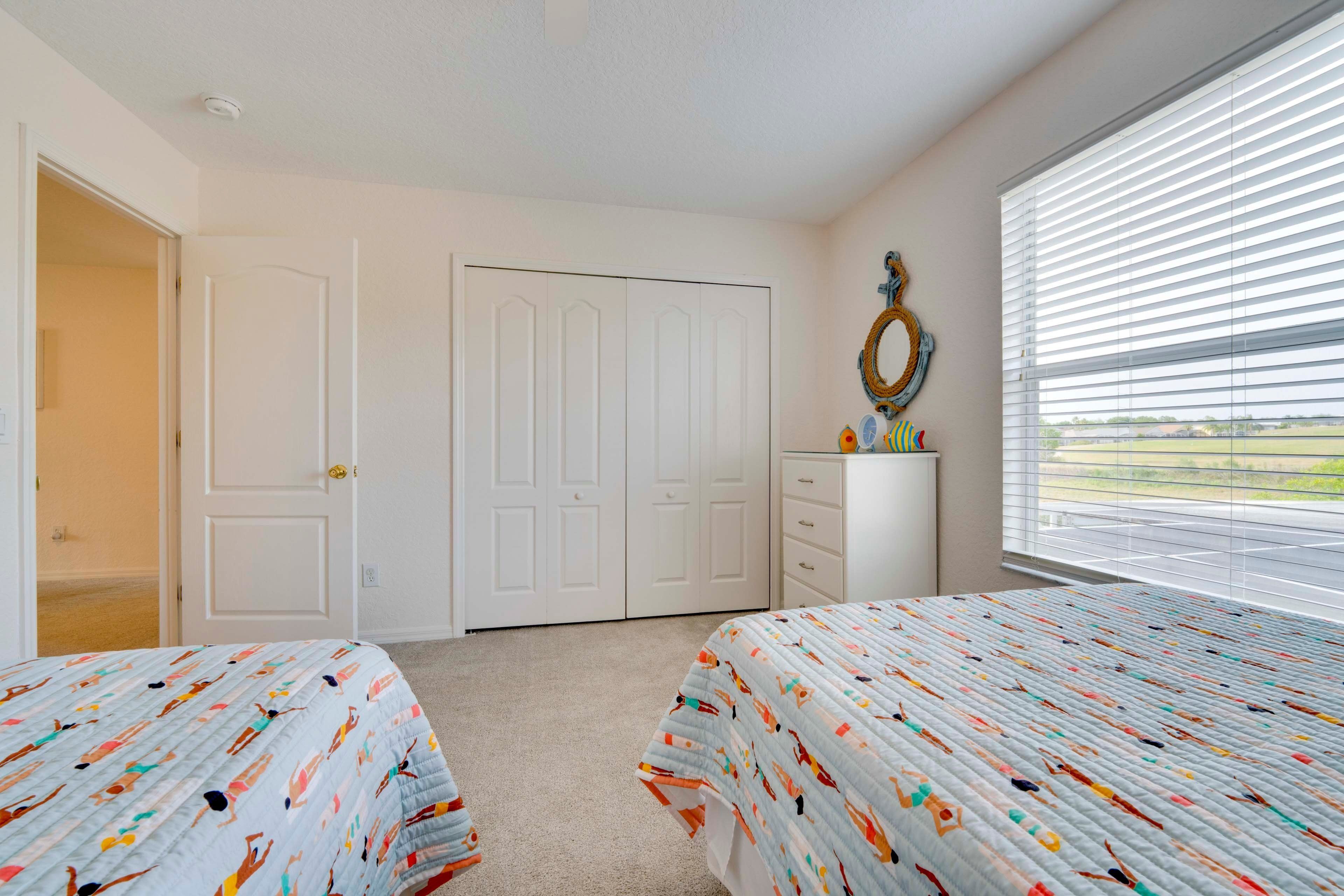 A bedroom with two beds, a dresser, a mirror, and a door.