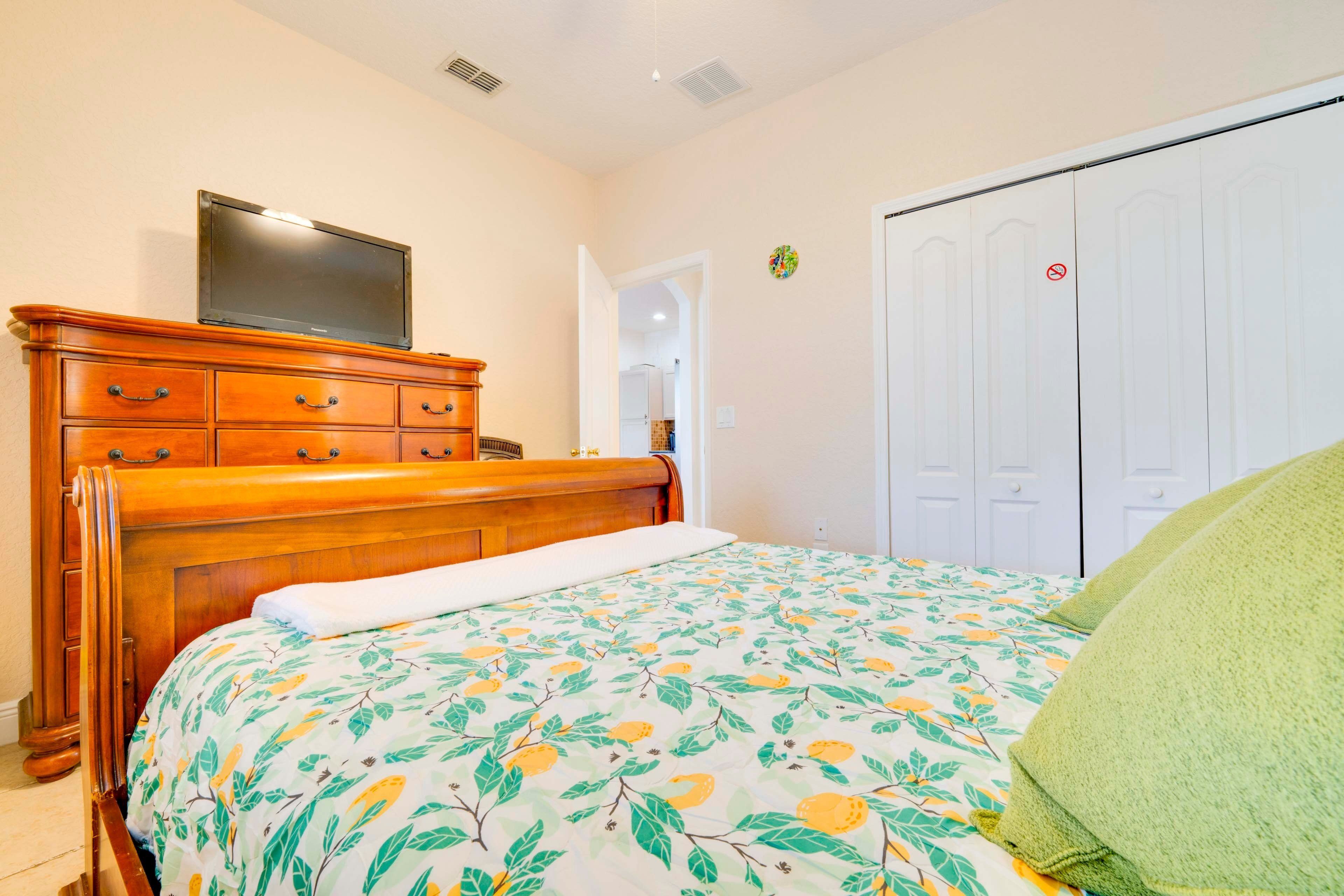 A bedroom with a wooden dresser, a bed with a floral bedspread, a television on the dresser, and a white wardrobe with a red prohibition sign.