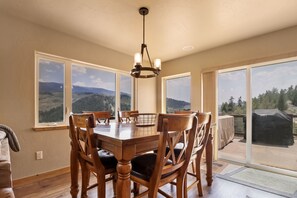 A dining area with a wooden table and chairs, large windows with a mountain view, and a ceiling light fixture. - 947 Blue Ridge 4 Bedroom Home (Silverthorne)