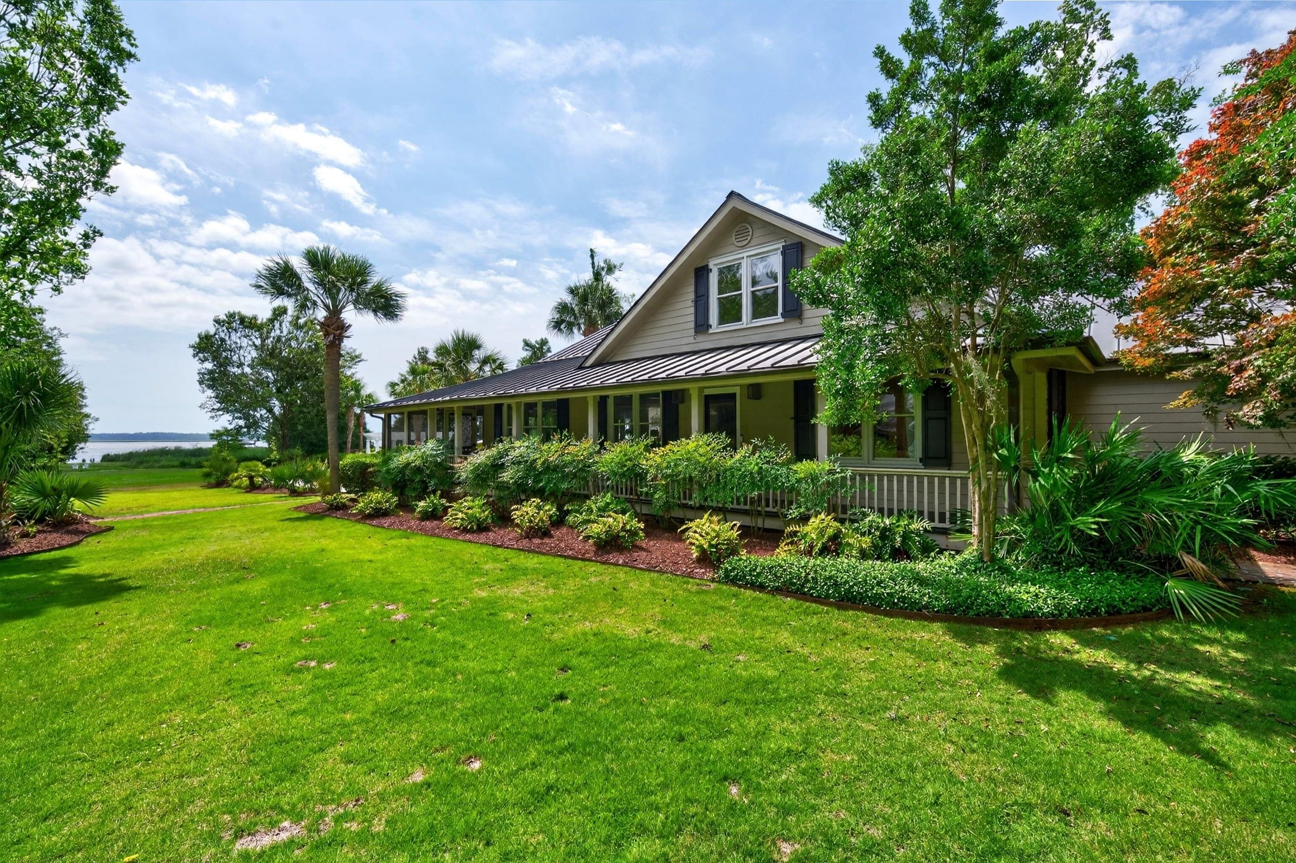 A two-story house with a covered porch, surrounded by a well-maintained lawn and various shrubs.