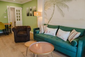 Ein Wohnzimmer mit einem grünen Sofa, einem braunen Sessel, einem kleinen runden Tisch und einem Essbereich mit einem gelben Stuhl.