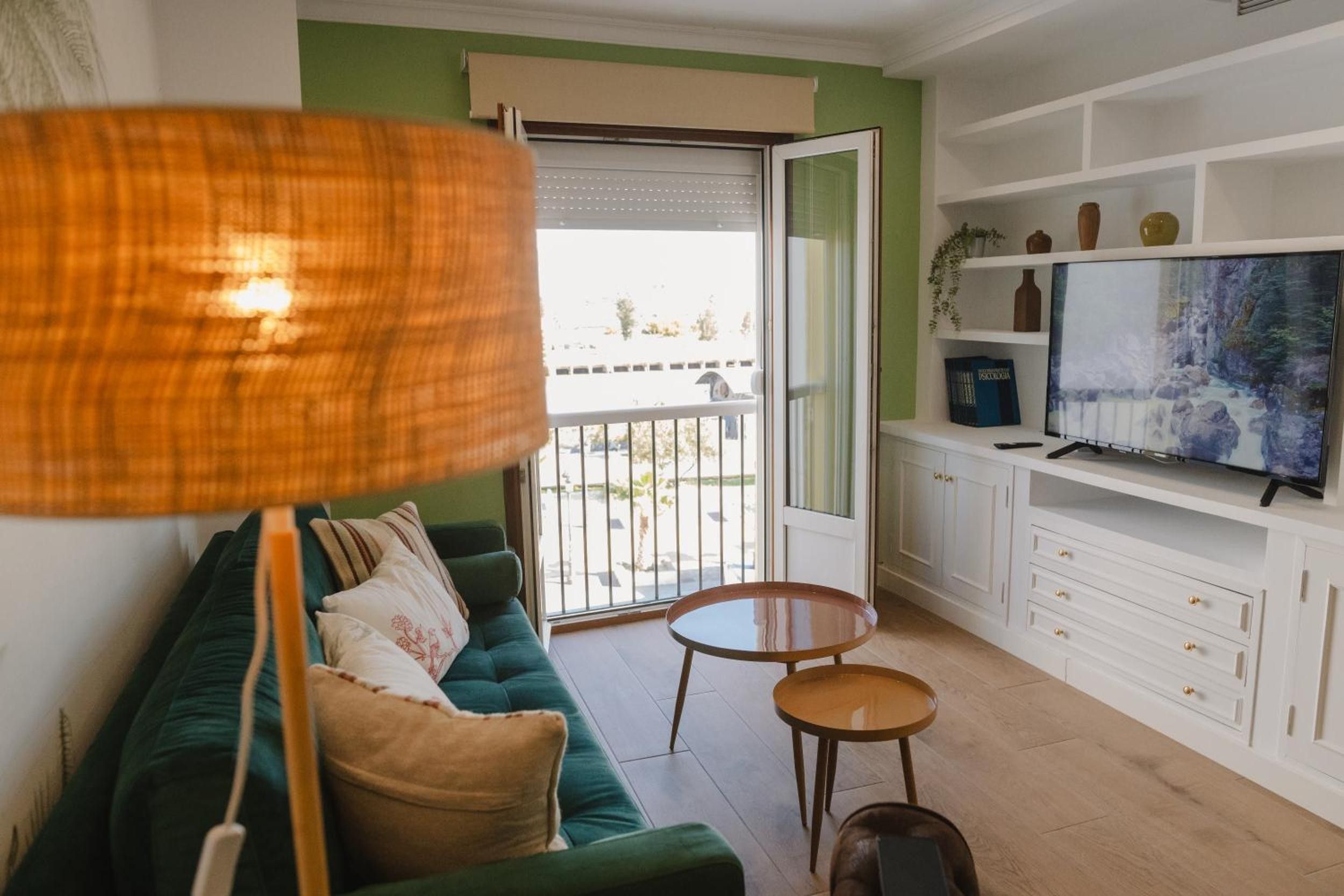 Una sala de estar con un sofá verde, un televisor, una mesita de madera y un balcón con vistas.