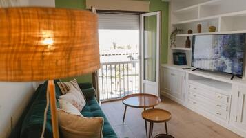 Una sala de estar con un sofá verde, un televisor, una mesita de madera y un balcón con vistas.