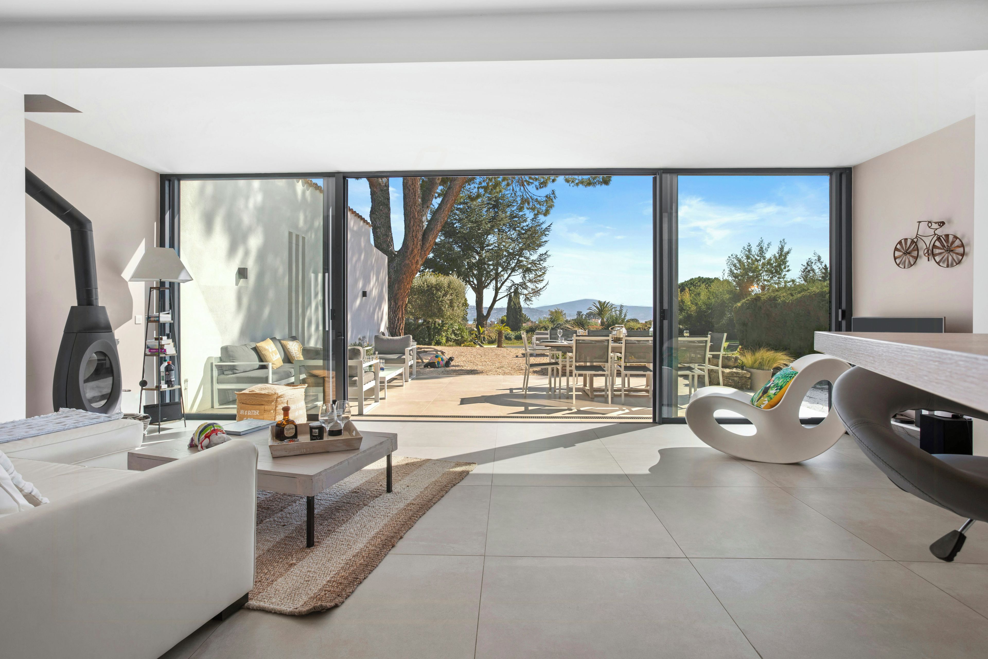 Un salon moderne comprenant un canapé, une table basse et un fauteuil original, qui donne sur une terrasse aménagée avec du mobilier d’extérieur et offrant une vue sur le paysage.