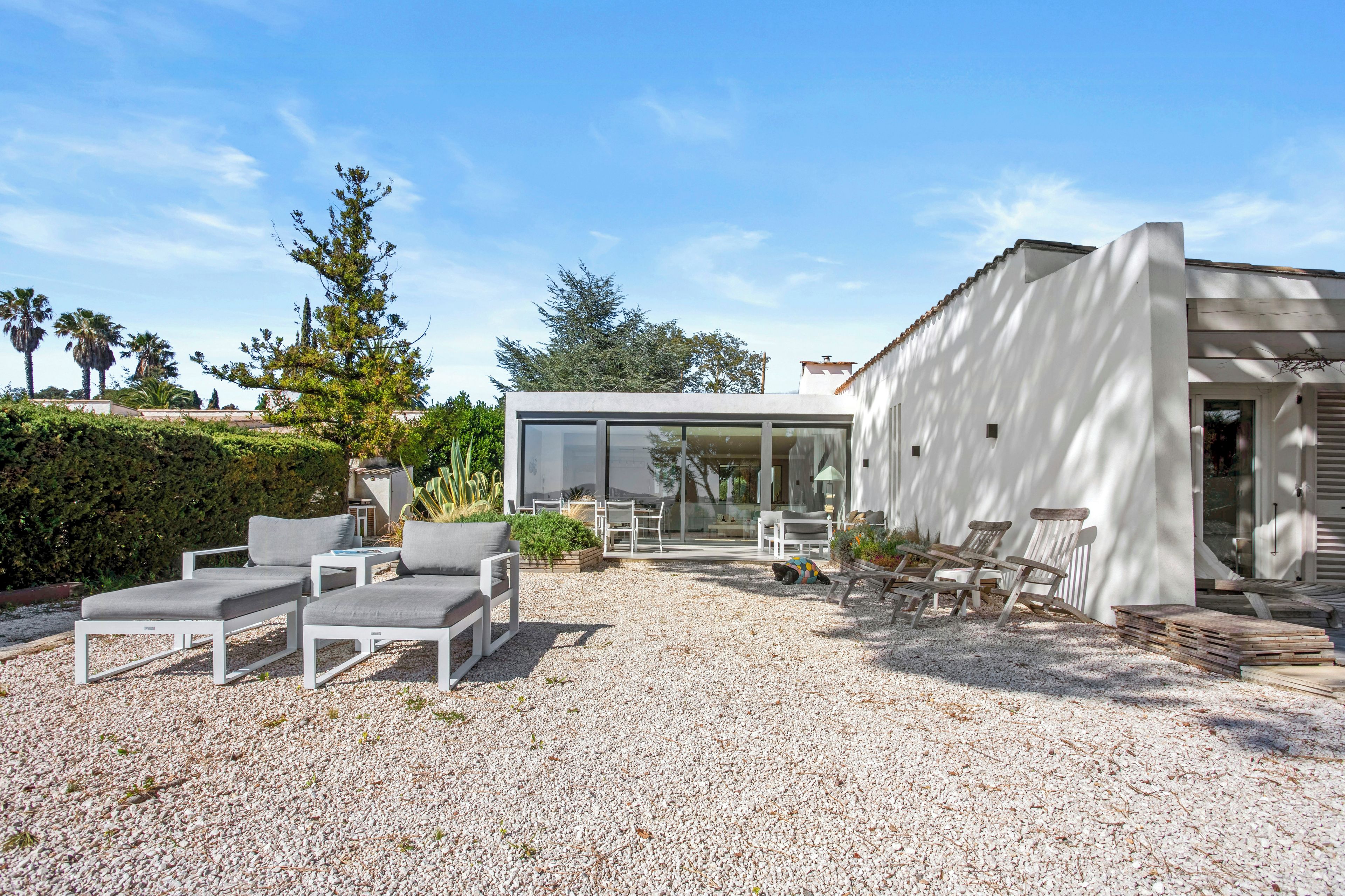 A modern outdoor seating area with white furniture, a gravel ground, and a building with large windows.