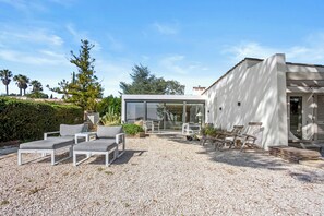 A modern outdoor seating area with white furniture, a gravel ground, and a building with large windows. - Villa with views over the Gulf of St-Tropez (Grimaud)