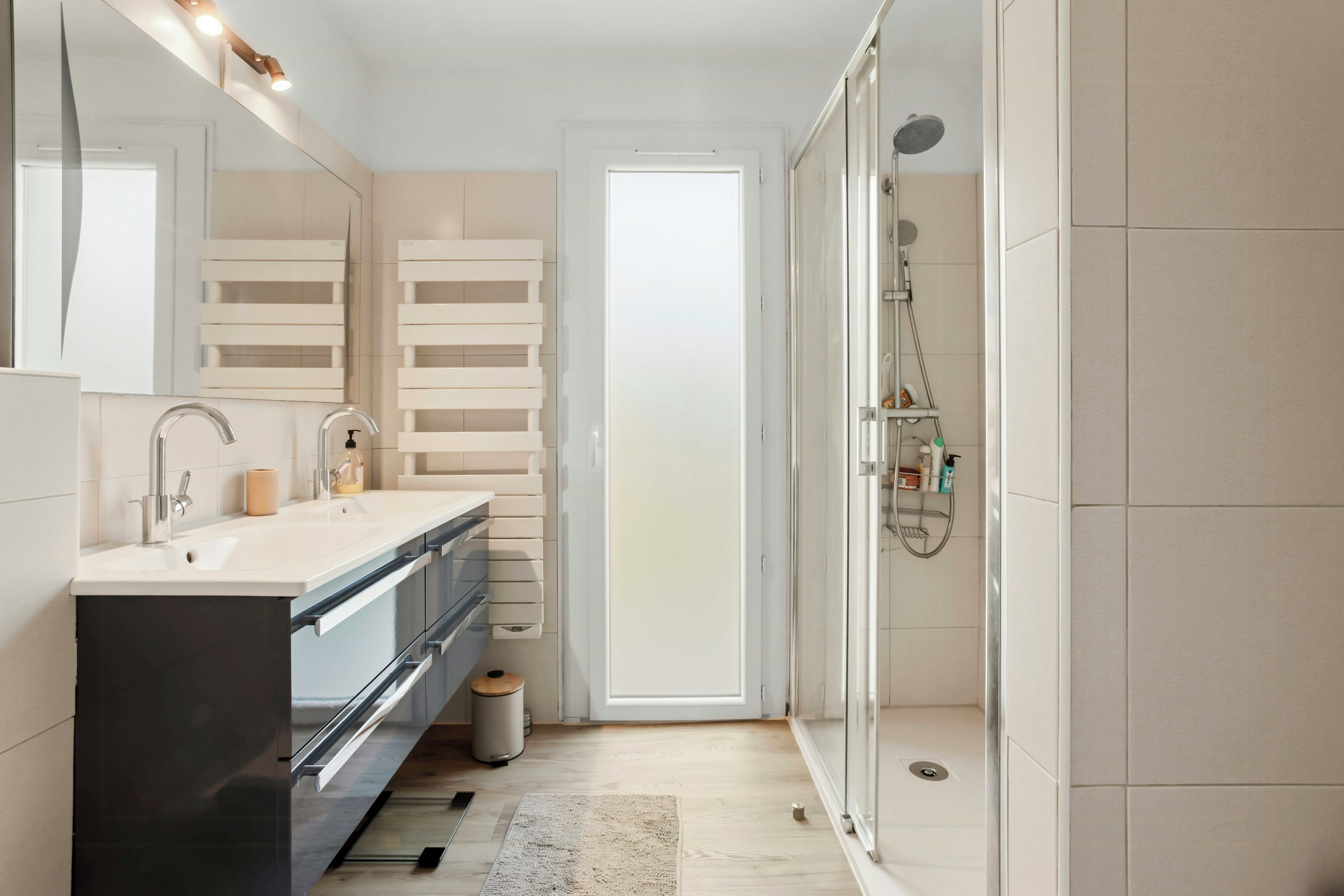 Une salle de bain moderne avec un meuble-lavabo à deux vasques, une douche et une porte en verre donnant sur une autre pièce.