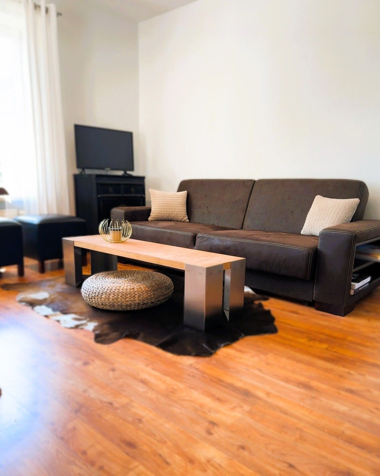 Ein Wohnzimmer mit einem braunen Ledersofa, einem Holztisch und einem Fernseher auf einem schwarzen Standfuß.