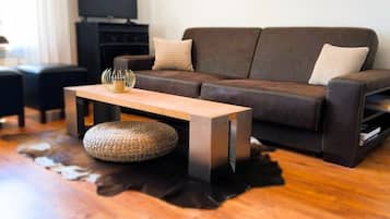 Ein Wohnzimmer mit einem braunen Ledersofa, einem Holztisch und einem Fernseher auf einem schwarzen Standfuß.