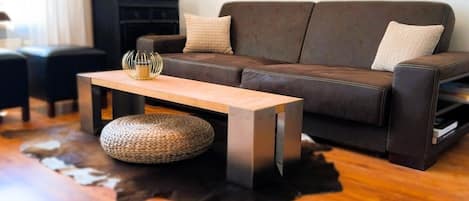 Ein Wohnzimmer mit einem braunen Ledersofa, einem Holztisch und einem Fernseher auf einem schwarzen Standfuß.