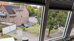 A view from a window overlooking a parking lot, a building with solar panels, and a tree. - Apartment in A Hotel 'Blickallee' (Havixbeck)