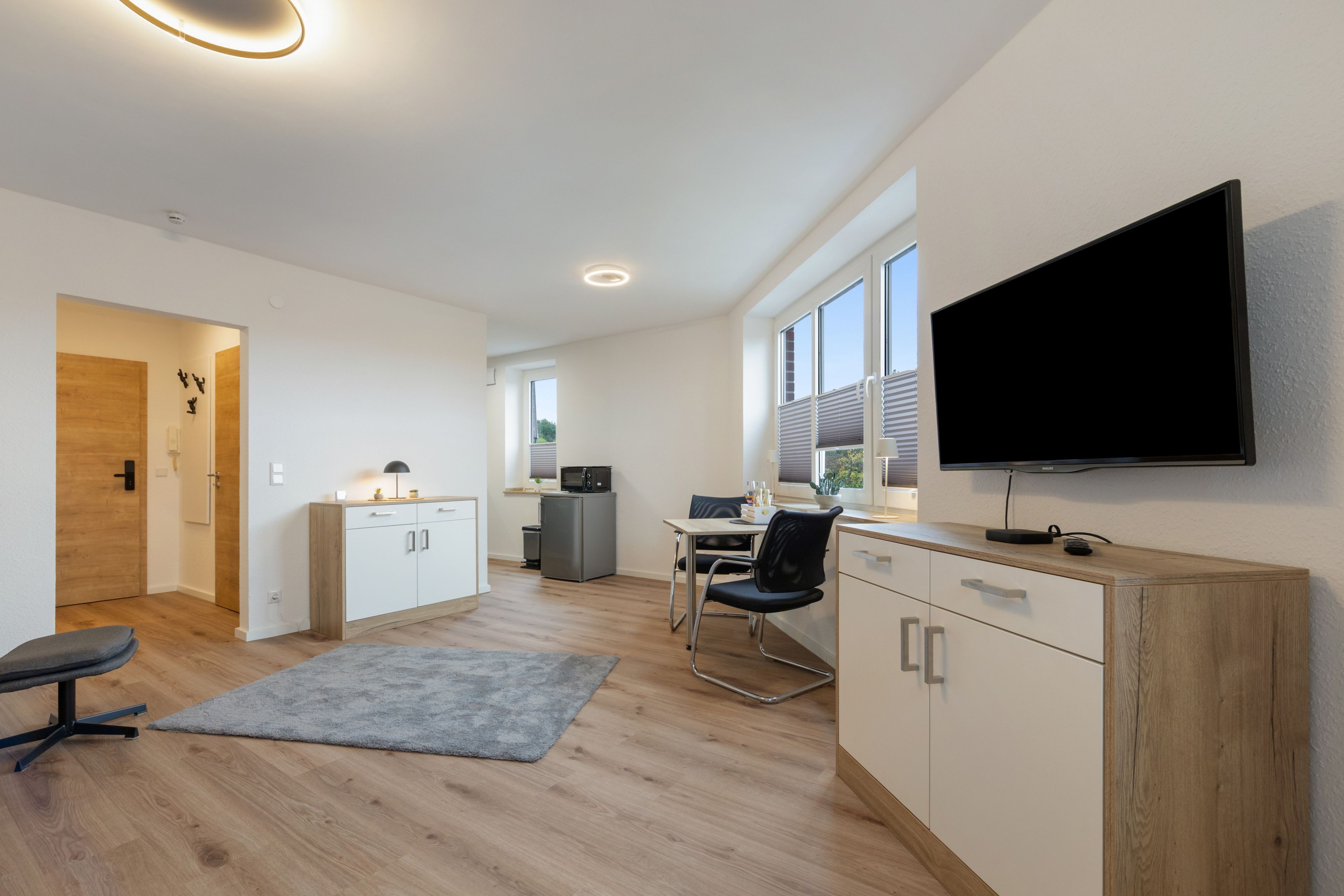 Ein modernes, helles Zimmer mit einem Flachbildfernseher, einer Küchenzeile, einem Essbereich und einer Sitzecke mit grauem Teppich.