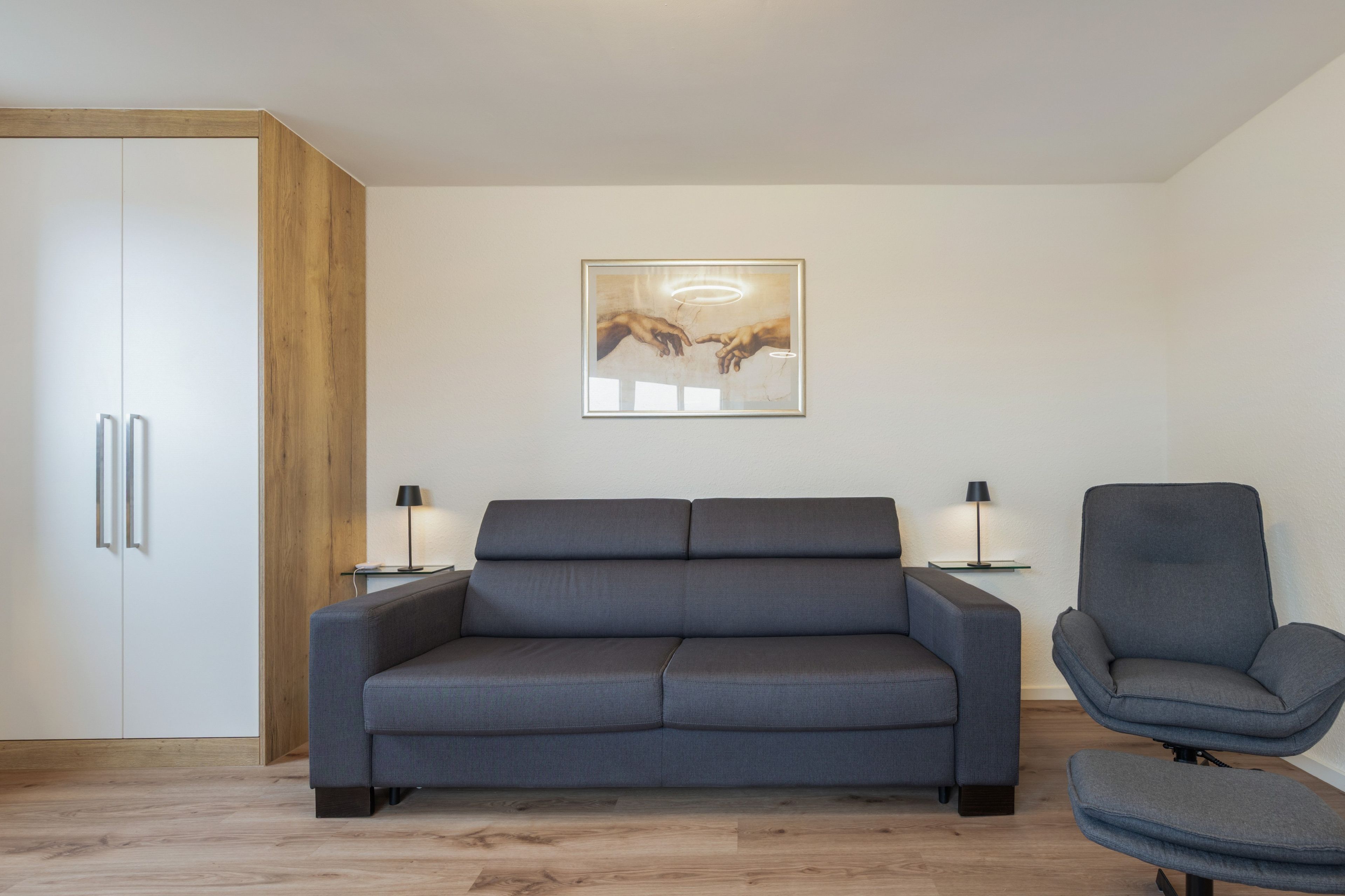 Ein modernes Wohnzimmer mit einem grauen Sofa, einem grauen Sessel und einem Holzschrank.