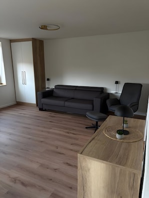 Ein modernes Wohnzimmer mit einem grauen Sofa, einem schwarzen Sessel und einem Holztisch.