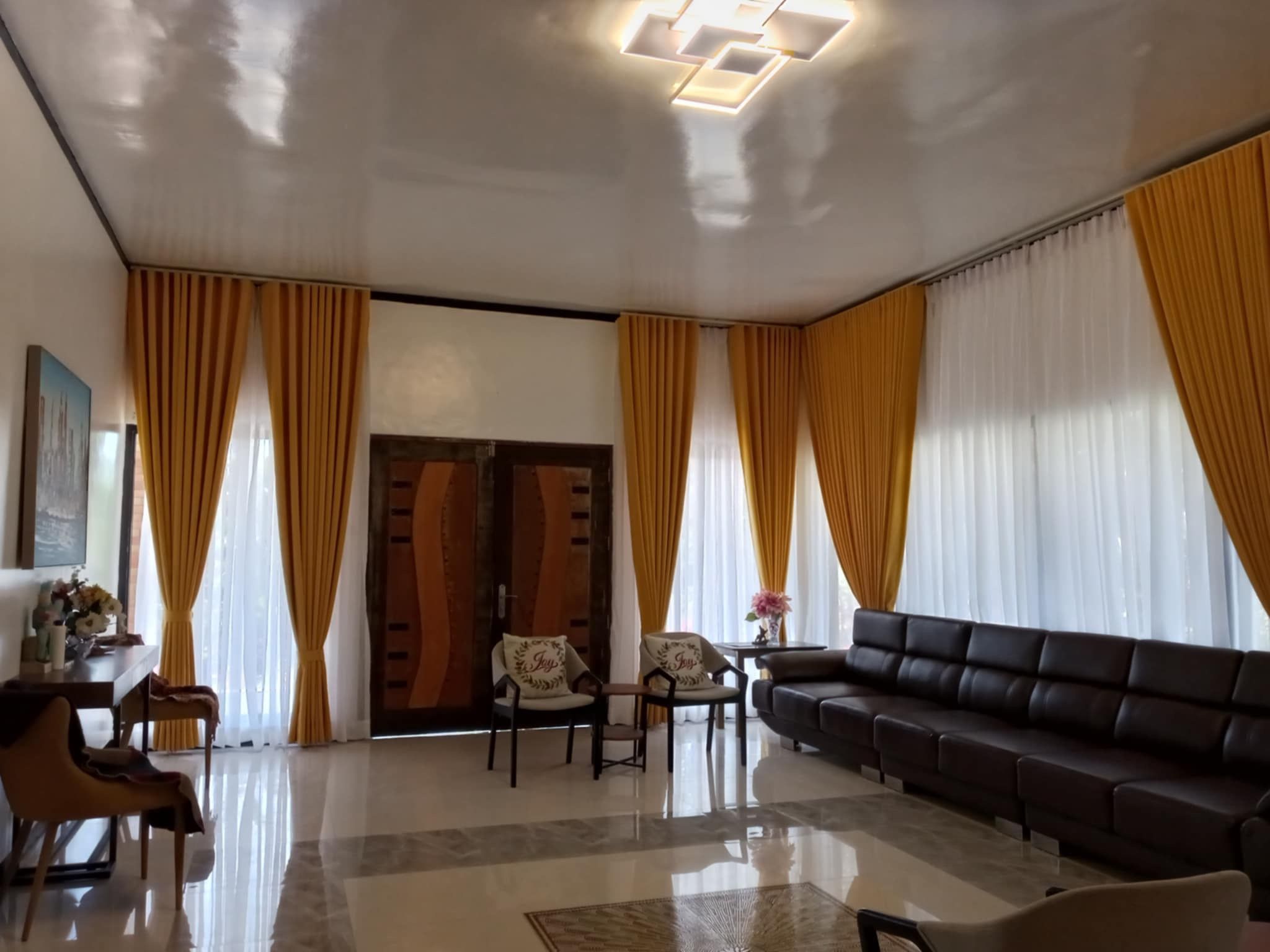 A spacious living room with a large sofa, two armchairs, a coffee table, and a dining area with a table and chairs.