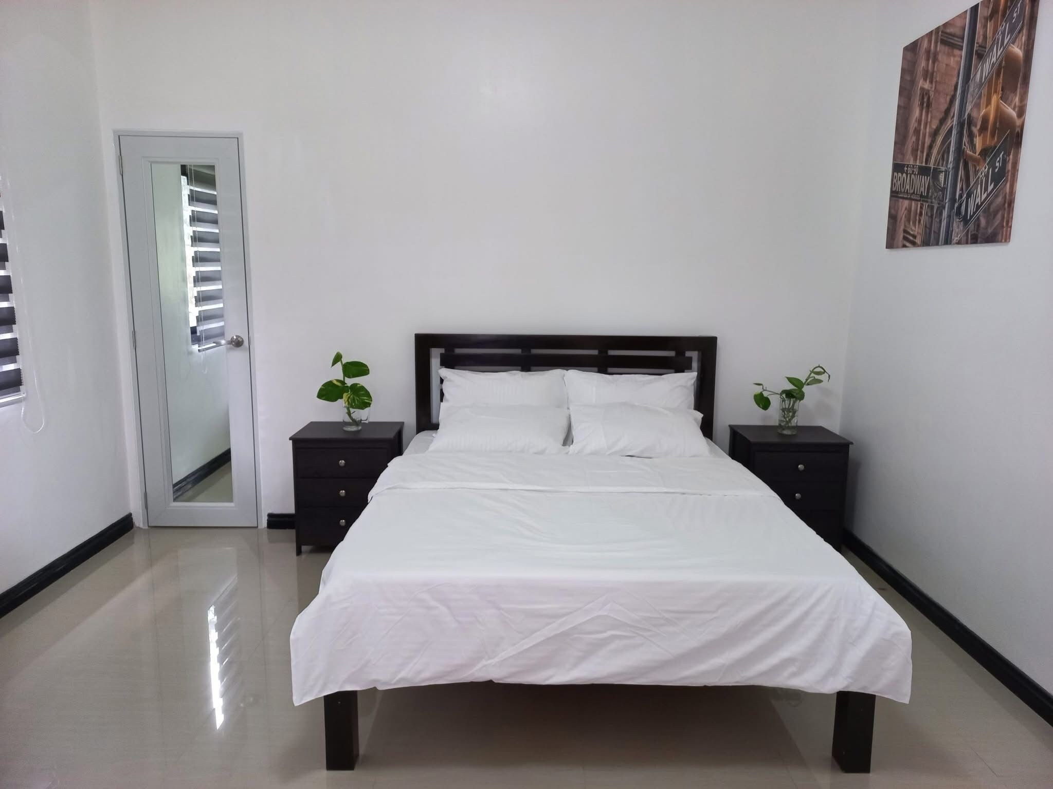 Un dormitorio con cama, dos mesitas de noche, una puerta y una obra de arte colgada en la pared.