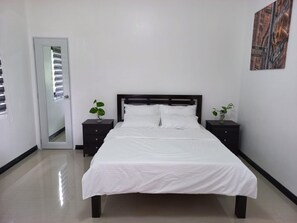 Un dormitorio con cama, dos mesitas de noche, una puerta y una obra de arte colgada en la pared.