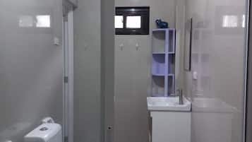 Un baño moderno con cabina de ducha de vidrio, inodoro, lavamanos y una ventana pequeña.