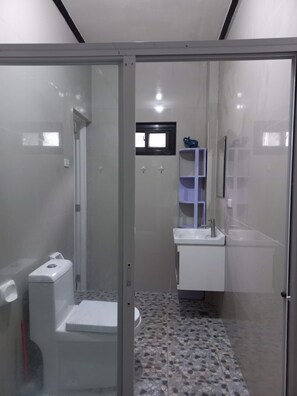 Un baño moderno con cabina de ducha de vidrio, inodoro, lavamanos y una ventana pequeña.