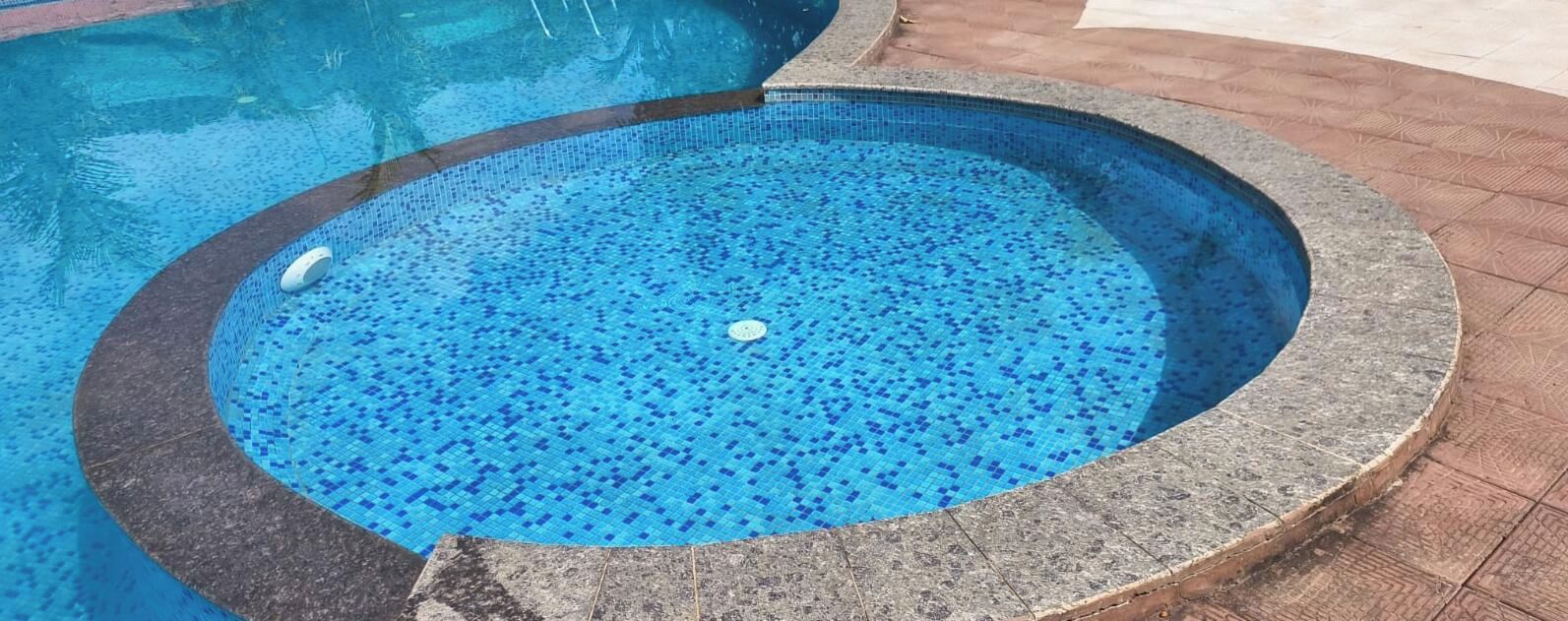 A circular hot tub with a tiled floor, surrounded by a stone border.