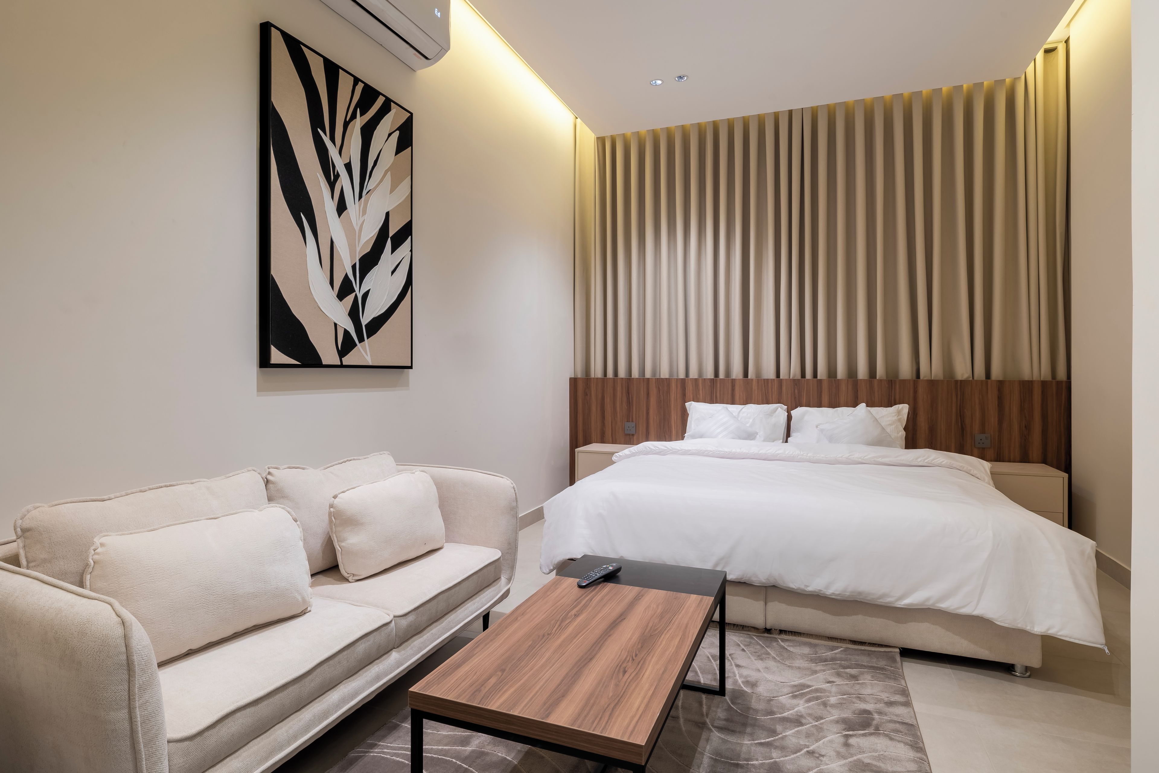 A modern hotel room with a bed, a sofa, a coffee table, and a large abstract painting.