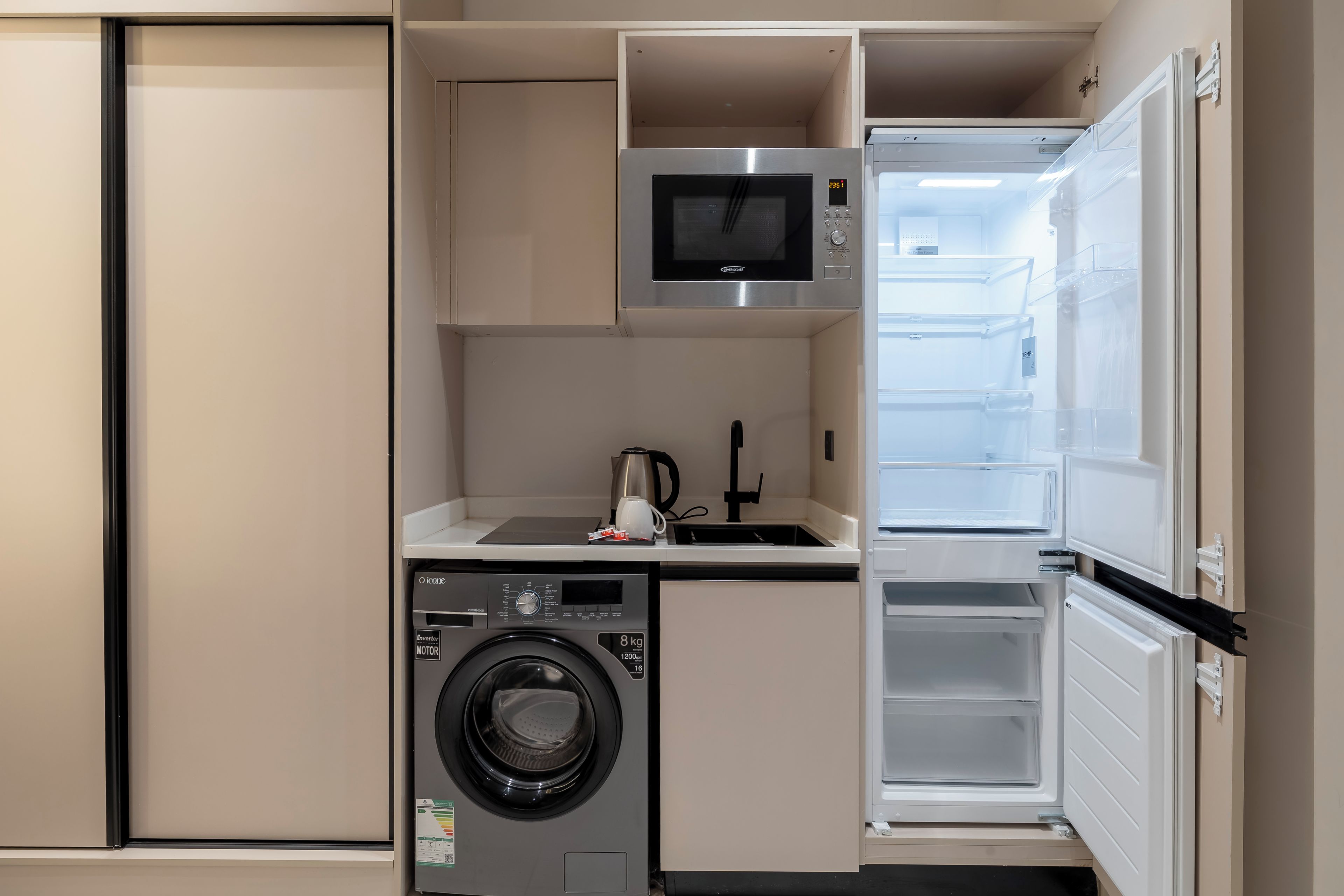 A compact kitchenette with a washing machine, a microwave, and a refrigerator.