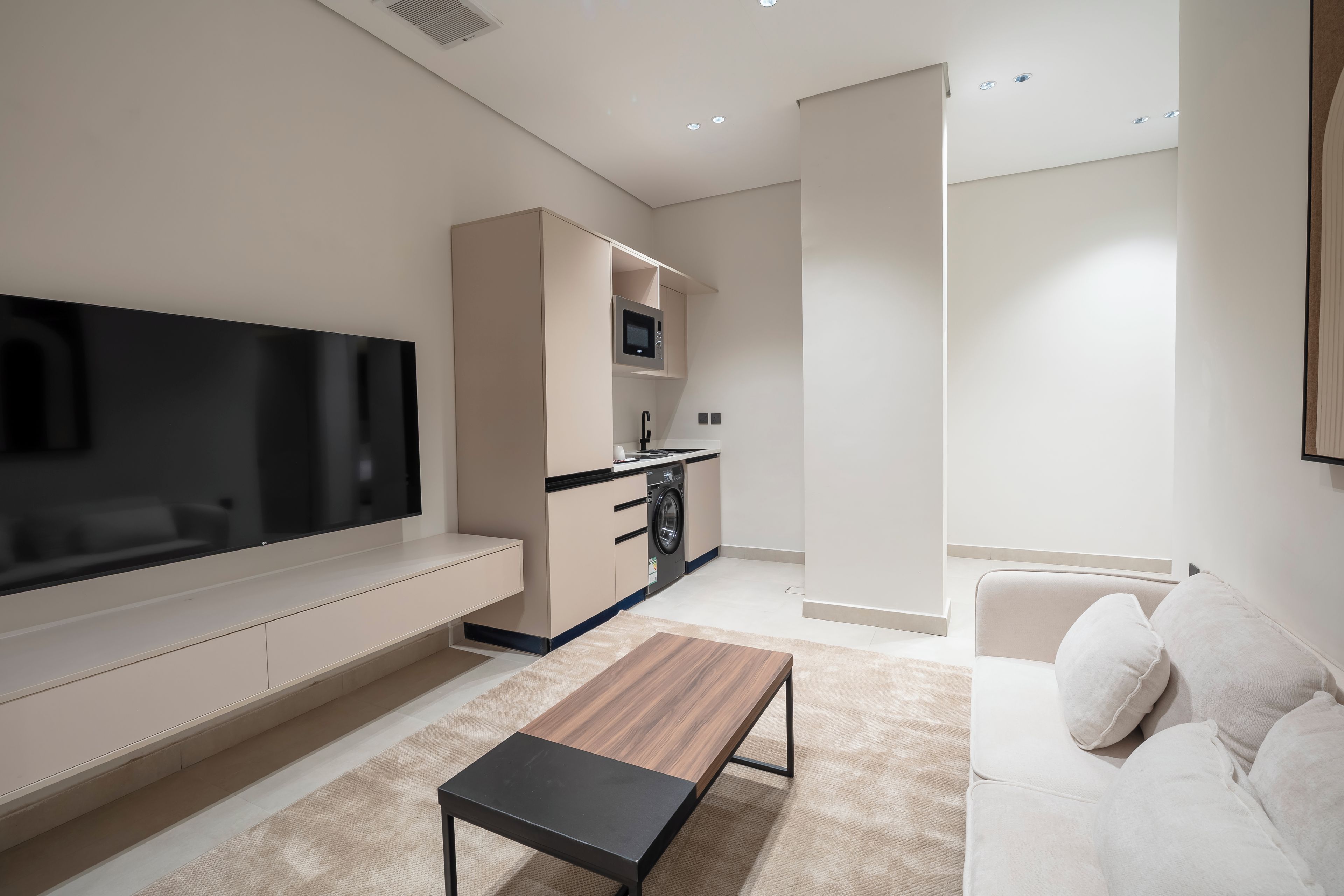 Una sala de estar moderna con un televisor de pantalla plana, un sofá, una mesa de centro y una zona de cocina con microondas.