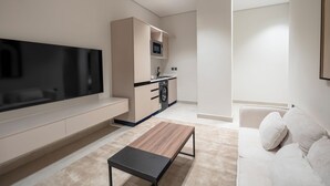 Una sala de estar moderna con un televisor de pantalla plana, un sofá, una mesa de centro y una zona de cocina con microondas.