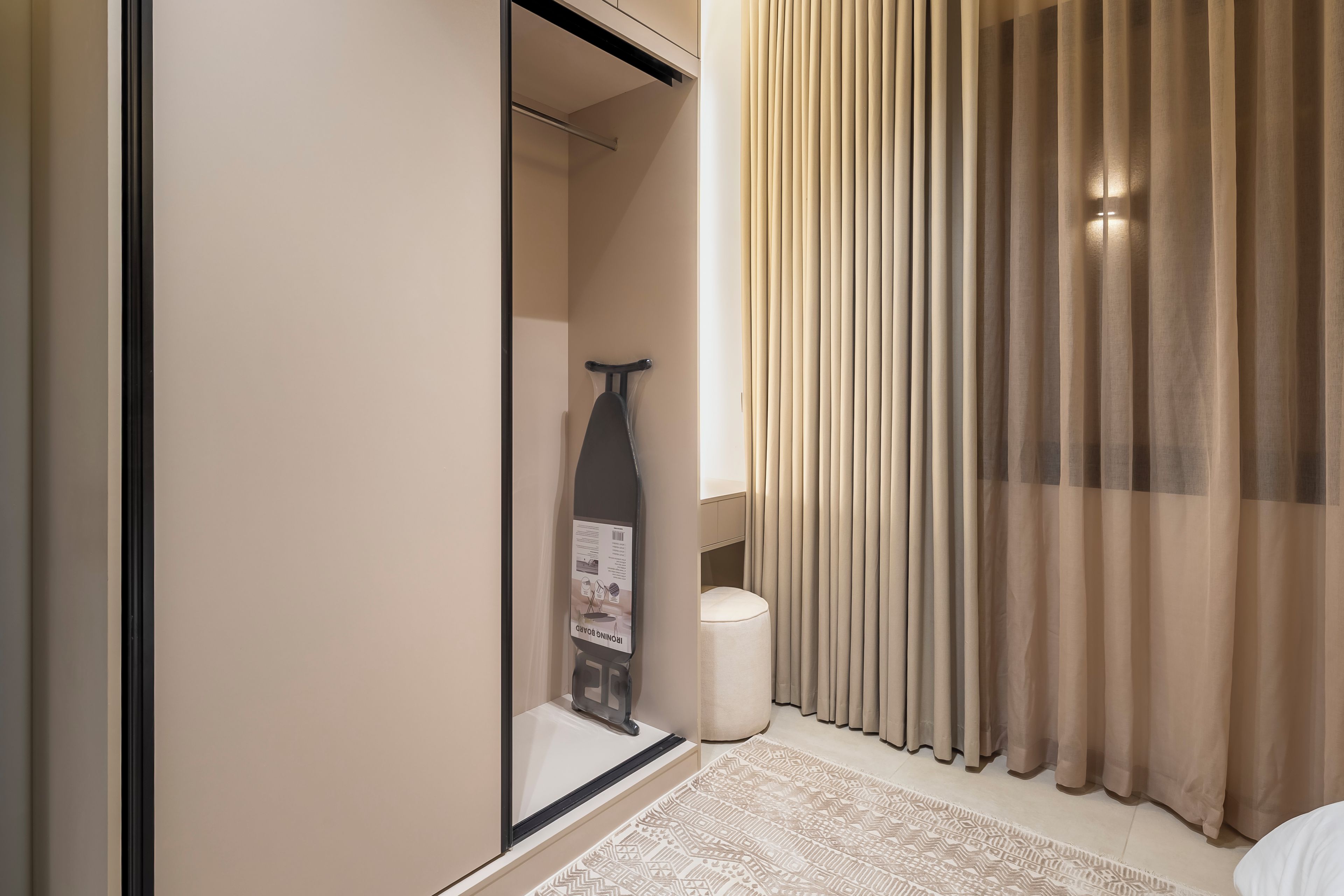 Habitación de hotel con puerta corrediza, una mesita con una botella, un objeto decorativo y una alfombra estampada.