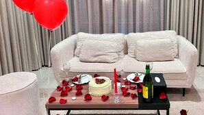 Una habitación con un sofá blanco, una mesa de comedor con un pastel y velas, y una botella de vino.
