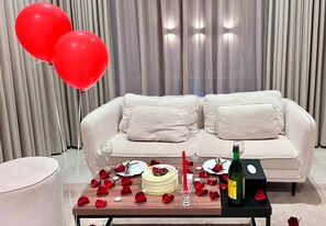 Una habitación con un sofá blanco, una mesa de comedor con un pastel y velas, y una botella de vino.