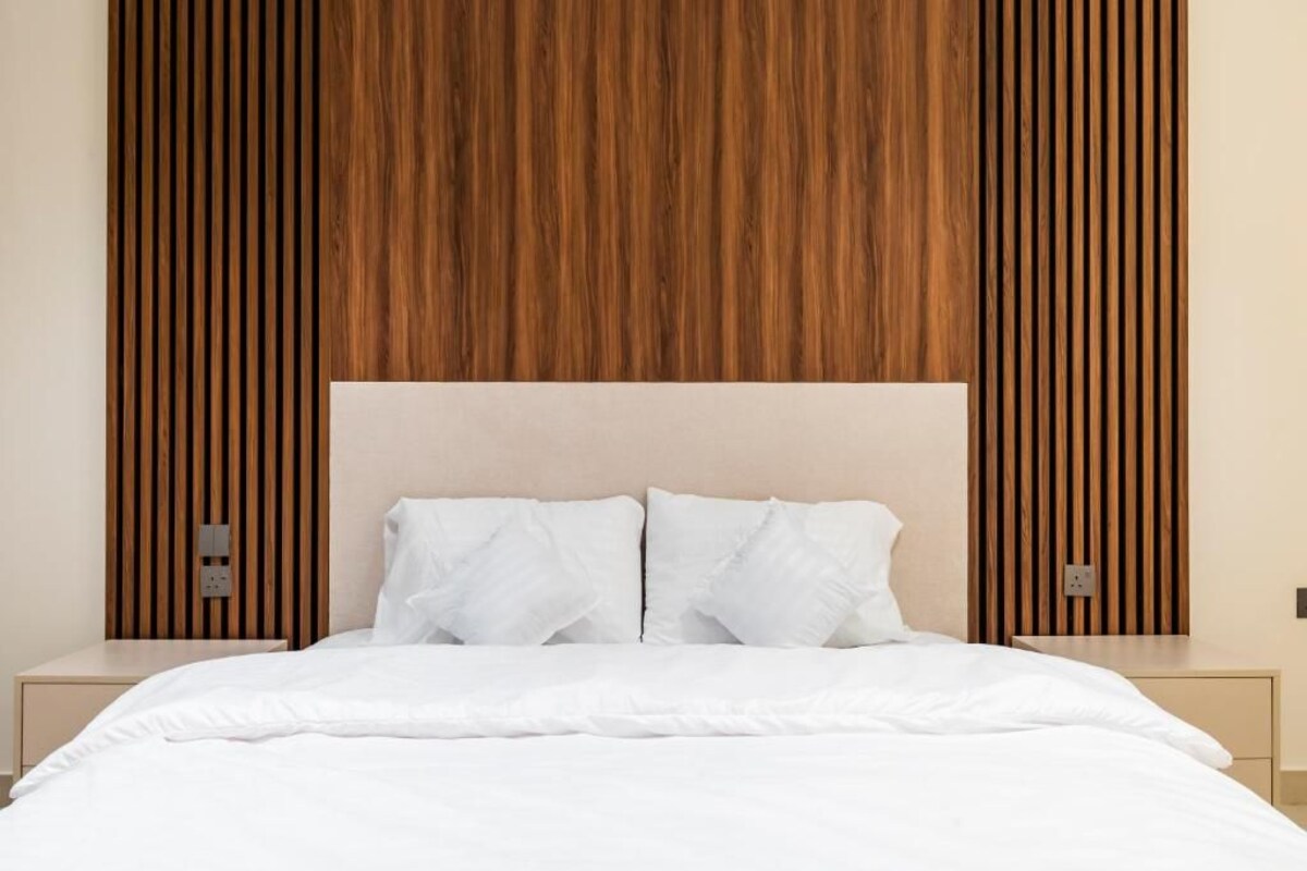 Una cama con ropa blanca, un cabecero de madera y dos mesitas de noche.