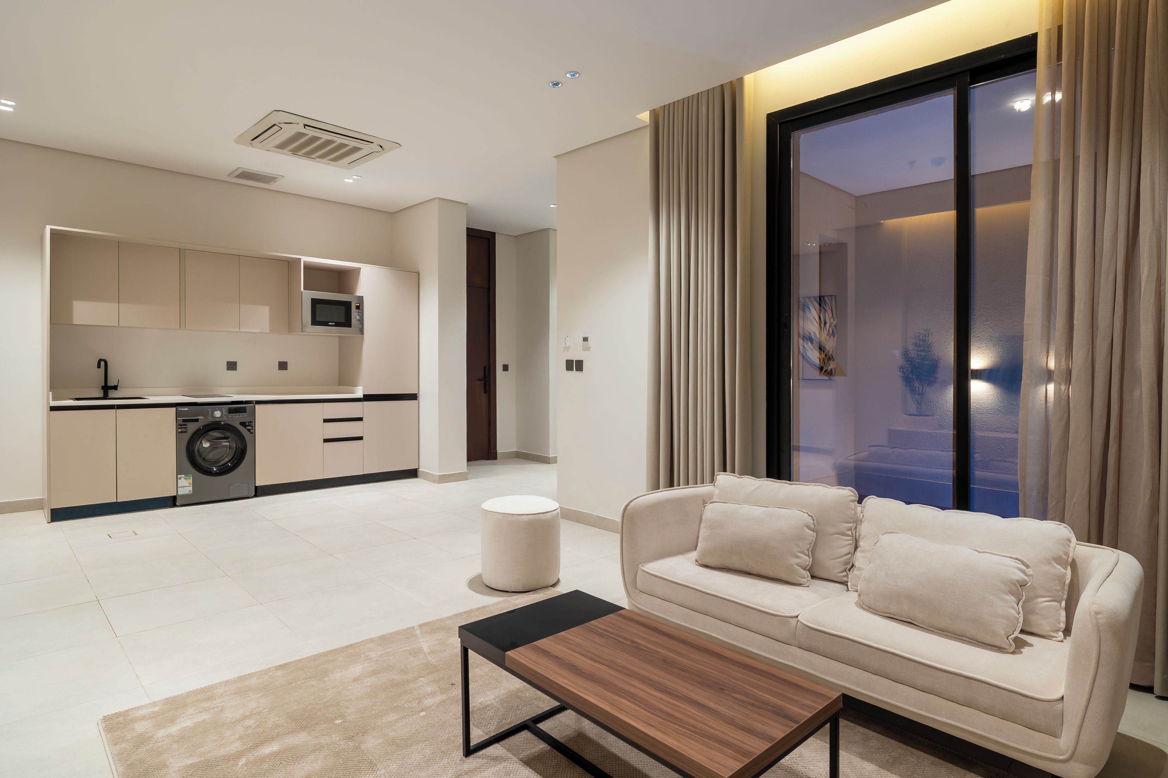 A modern living room with a sofa, a coffee table, and a kitchen area in the background.