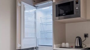 Cocina compacta con microondas integrado, hervidor y refrigerador con varios estantes.